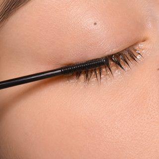 Close-up of a black mascara wand applying black eyelash serum or mascara to a person's eyelashes.