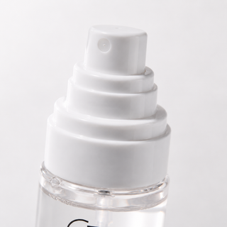 Close-up of a white pump dispenser bottle with a clear lower section and a small black logo, photographed on a light gray background.