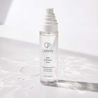 A clear cylindrical bottle of Cpretty BHA Exfoliating Toner with a white pump dispenser, set on a glossy white surface with artistic water ripple shadows.