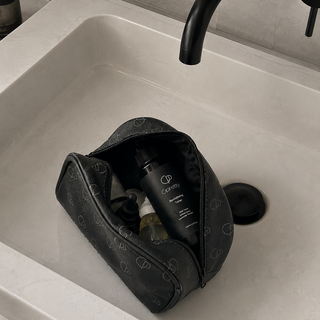 Black toiletry bag with products on a bathroom sink