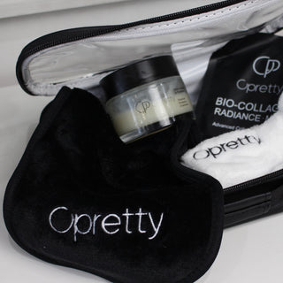 Opretty branded travel set including a black zippered bag, black pouch, white towel, and a small jar, arranged on a white surface.