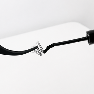 Close-up of a black mascara wand with a single lash cluster being coated on a clean white background.